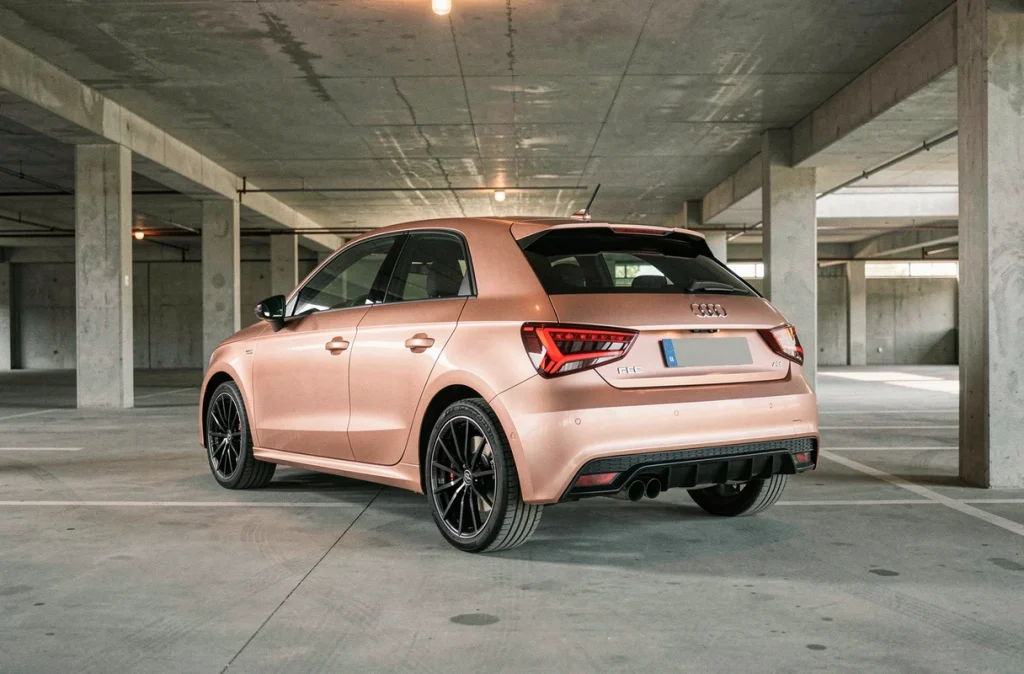 Audi A1 entièrement wrappée en rose gold photographiée de trois-quarts arrière dans un parking en béton moderne