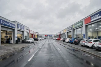 Vue panoramique d'une zone commerciale automobile dans les Côtes-d'Armor avec plusieurs garages et concessionnaires sous un ciel breton nuageux
