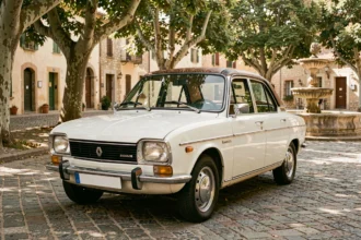 Renault 8 blanche des années 60 garée sur une place de village provençale en 2026, vue en angle 3/4 avant sur pavés